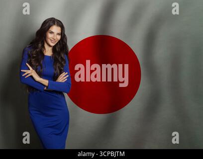 Fröhliche junge Frau in blauem Kleid lächelt vor japanischem Flaggenhintergrund Stockfoto