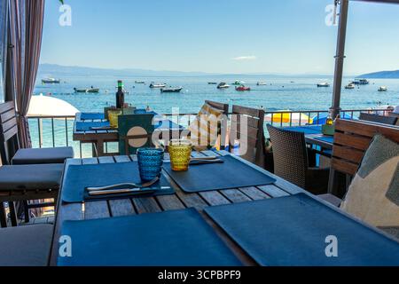 Seestrand-Café-Terrasse mit Tischen und Meerblick, Strandschirme und Boote in der Nähe Stockfoto