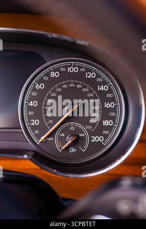 Klassischer analoger Tachometer, der Meilen und Kilometer pro Stunde in einem modernen Luxusauto mit Chrom- und Holzverkleidung anzeigt Stockfoto