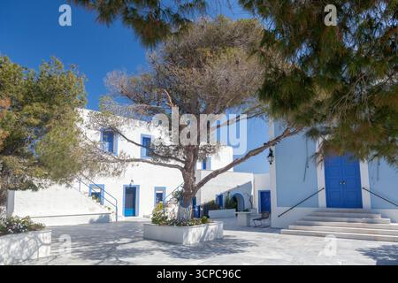 Wunderschöne griechisch-orthodoxe Kapelle von Panagia Kastriani, auf der Insel Kea, mit einer blauen Kuppel und einem Glockenturm, eingerahmt von Bäumen vor einem klaren blauen Himmel. Stockfoto