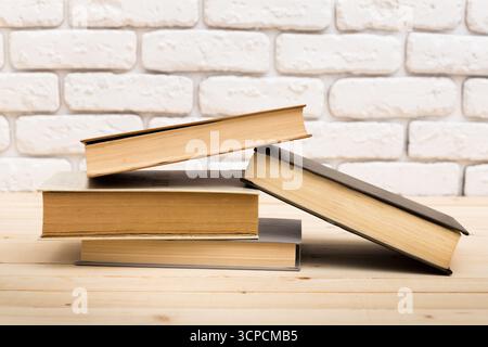 Gestapelte Bücher auf einem Holztisch vor einer Backsteinmauer Stockfoto