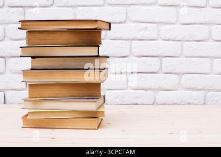 Stapelte Bücher auf Holzoberfläche vor einer weißen Ziegelwand in gemütlicher Umgebung Stockfoto