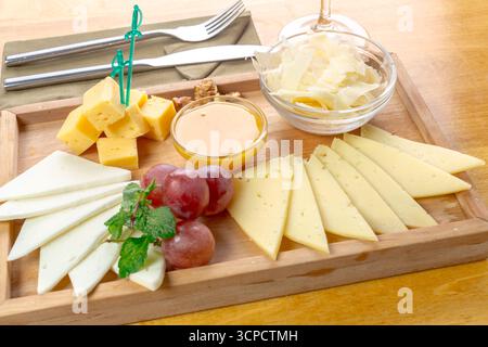 Käseplatte mit verschiedenen Käsesorten, Trauben und Honig auf einem hölzernen Servierbrett Stockfoto