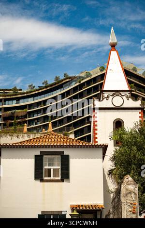 Ein traditionelles weißes Gebäude mit einem rot gekachelten Dach und einem kirchenähnlichen Turm steht in krassem Kontrast zu einem modernen, geschwungenen Hotel- oder Wohnkomplex Stockfoto