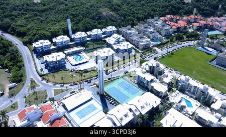 Blick aus der Vogelperspektive auf Praia Brava in Florianópolis mit mehreren Apartmentkomplexen und Sommerhäusern vor dem Strand, umgeben von Bergen Stockfoto