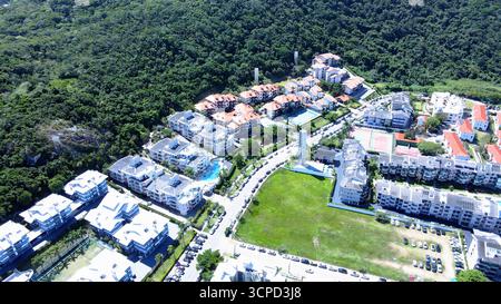 Blick aus der Vogelperspektive auf Praia Brava in Florianópolis mit mehreren Apartmentkomplexen und Sommerhäusern vor dem Strand, umgeben von Bergen Stockfoto