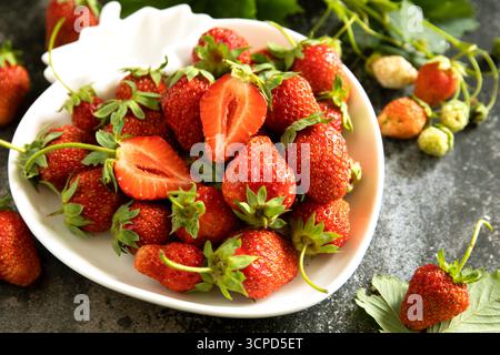 Frische Sommererdbeeren in weißer Schüssel auf dunkler rustikaler Oberfläche. Stockfoto