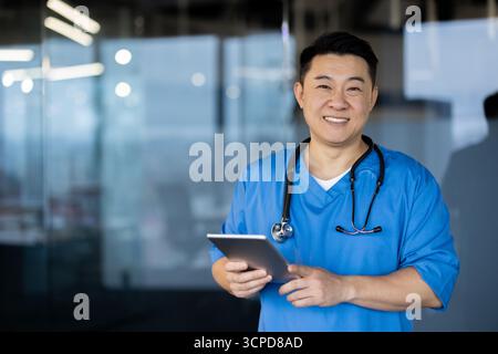 Porträt eines jungen asiatischen männlichen Arztes und medizinischen Personals, der in einer Klinik in Uniform mit einem Stethoskop steht, eine Tablette hält und die Kamera lächelt. Stockfoto