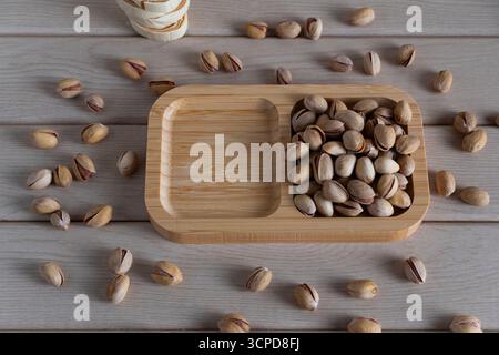 Blick von oben auf rustikale Pistazien auf einem Holztablett, verstreut auf einer hellen Holzoberfläche, die natürliche Texturen und Erdtöne hervorhebt Stockfoto