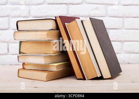 Gestapelte Bücher mit verschiedenen Einlagen, die auf einem Holztisch gegen eine Ziegelwand ruhen Stockfoto