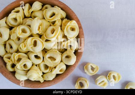 Rohe hausgemachte Tortellini in einer Holzschale auf grauem Hintergrund. Traditionelles italienisches Essenskonzept. Selektiver Fokus. Horizontale Ausrichtung. Draufsicht. Co Stockfoto