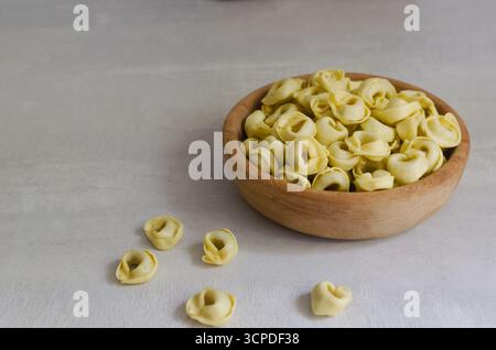Rohe hausgemachte Tortellini in einer Holzschale auf grauem Hintergrund. Traditionelles italienisches Essenskonzept. Selektiver Fokus. Horizontale Ausrichtung. Kopierbereich Stockfoto