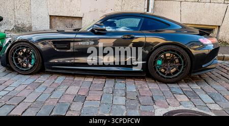 Schwarzer Mercedes-AMG GT Sportwagen, der auf einer Kopfsteinpflasterstraße in Tallinn, Estland, geparkt ist und in seiner polierten Karosserie die Architektur der Altstadt widerspiegelt. Stockfoto