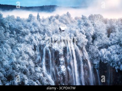 Blick aus der Vogelperspektive auf Wasserfall, Haus und verschneiten Wald im Winter Stockfoto