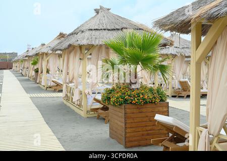 Gemütliche hölzerne Strandhütten mit weißen Vorhängen am Strand oder Resort. Bungalow für private Erholung am sonnigen Sommertag. Stockfoto
