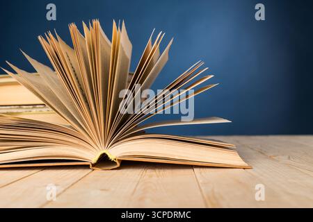 Öffnen Sie das Buch, das seine Seiten vor blauem Hintergrund auf einem Holztisch zeigt Stockfoto