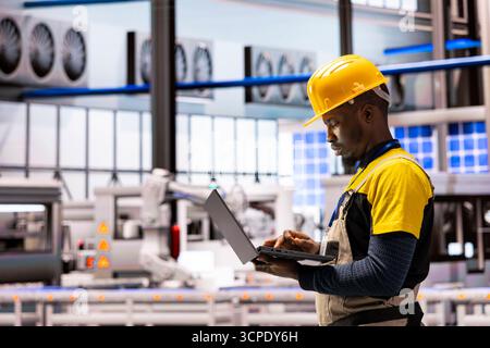 Afroamerikanischer Ingenieur überprüft Anlagen in Industrieanlagen und überwacht automatisierte Montagelinien und Roboterarme. Männlicher Techniker nimmt Inventar der intelligenten Fertigung in Industrie 4,0 auf. Stockfoto