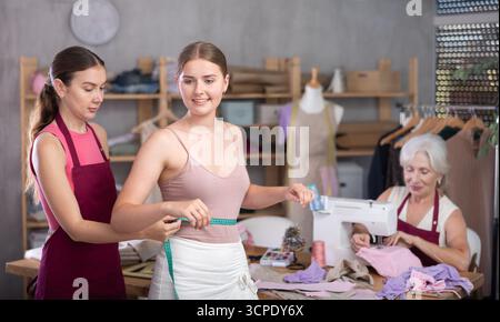 Eine Erwachsene Schneiderin nimmt Messungen für einen Kunden in der Werkstatt vor Stockfoto