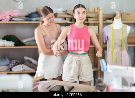 Junge Schneiderin nimmt Körpermaße von erwachsenen Frauen Stockfoto