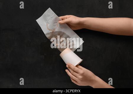 Frau wischt verschütteten Kaffee mit Papierserviette auf schwarzem Hintergrund ab Stockfoto