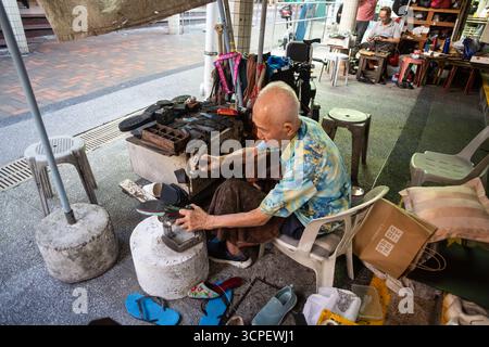 Chinesischer älterer Schuster repariert Schuhe auf der Straße unter Obdach, alter Mann arbeitet Ende 80 Die sterbende Handelsszene, Chinatown, Singapur. Stockfoto