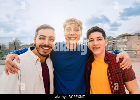 Multirassische männliche Freunde lachen und umarmen draußen im Stadtpark. Jugendfreundschaft und Lebensstil-Konzept Stockfoto
