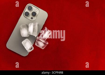 Das Konzept der Überhitzung und Brandgefahr. Kühlung des neuesten Smartphones mit Eiswürfeln. Zu hohe Betriebstemperatur des Prozessors beschädigt das iPhone Stockfoto