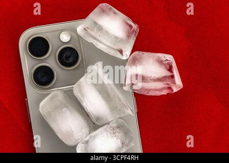 Das Konzept der Überhitzung und Brandgefahr. Kühlung des neuesten Smartphones mit Eiswürfeln. Zu hohe Betriebstemperatur des Prozessors beschädigt das iPhone Stockfoto
