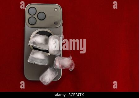 Das Konzept der Überhitzung und Brandgefahr. Kühlung des neuesten Smartphones mit Eiswürfeln. Zu hohe Betriebstemperatur des Prozessors beschädigt das iPhone Stockfoto