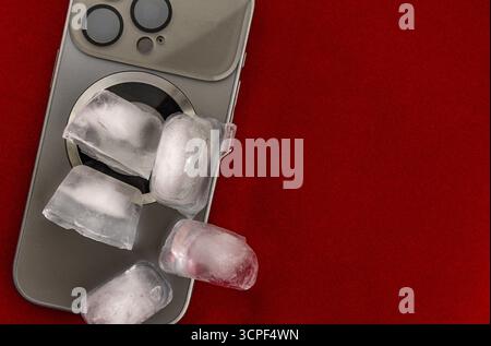 Das Konzept der Überhitzung und Brandgefahr. Kühlung des neuesten Smartphones mit Eiswürfeln. Zu hohe Betriebstemperatur des Prozessors beschädigt das iPhone Stockfoto