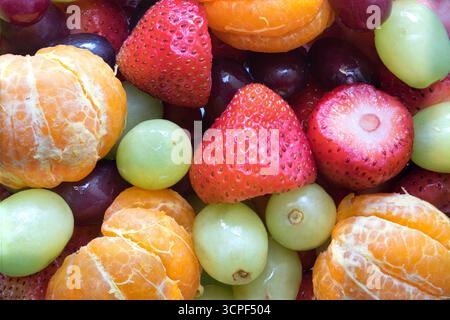 Obstsalat Mischung mit Erdbeeren, Trauben und geschälten Mandarinen flach gelegt voller Rahmen Hintergrund. Stockfoto