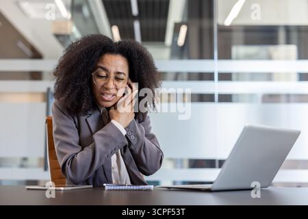 Afroamerikanische junge Frau mit Ohrenschmerzen, die an einem Schreibtisch im Büro sitzt und ihr Ohr mit der Hand hält. Stockfoto