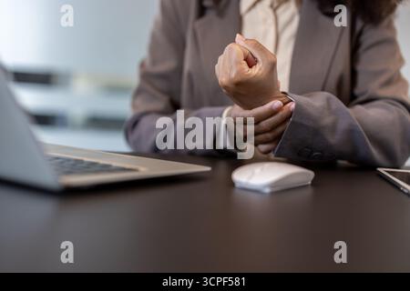 Nahaufnahme eines Körperteils einer jungen Afroamerikanerin in einem Anzug, die am Schreibtisch in einem Büro sitzt und ihr Handgelenk hält. Stockfoto