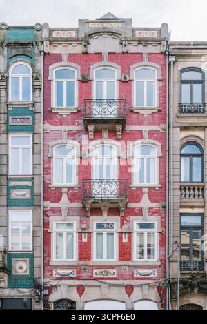 Eindrucksvolle Fassade des Porto-Gebäudes mit hellrotem Ziegelwerk und dekorativen Bogenfenstern in der historischen Innenstadt von Portugal. Traditionelle Architektur Stockfoto