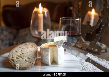 Der Käse Chaource, der in Scheiben mit Brot und Rotwein bei warmem Kerzenschein präsentiert wird, der typisch für die Champagne ist, besticht durch seine flauschige weiße Form Stockfoto