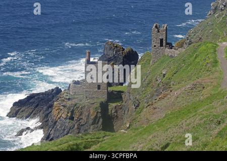 Historische Ruinen auf einer Klippe, umgeben von felsiger Küste und rauschenden Meereswellen, Maschinenraum einer alten Kupfermine in Cornwall, Großbritannien Stockfoto