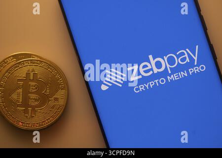 Bitcoin-Münze neben einem Smartphone mit dem Zebpay-Logo auf einem blauen Bildschirm Stockfoto