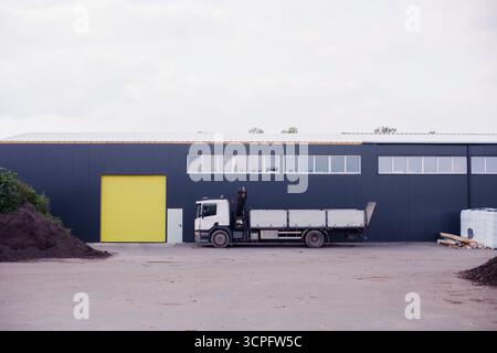 Großer langer Lkw mit offener Karosserie und Kranmanipulator, der vor Ort zwischen Sandpfählen geparkt ist Stockfoto