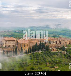 Blick aus der Vogelperspektive auf die historische Architektur und den Dom von Pienza eingebettet in sanfte grüne Hügel, umgeben von Nebel, Pienza, Toskana, Italien. Stockfoto