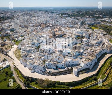 Aus der Vogelperspektive auf weiß getünchte Gebäude, die eng gruppiert sind und einen atemberaubenden Kontrast zum azurblauen Himmel schaffen, eine zeitlose Szene italienischer Architektur, Ostuni, Apulien, Italien. Stockfoto