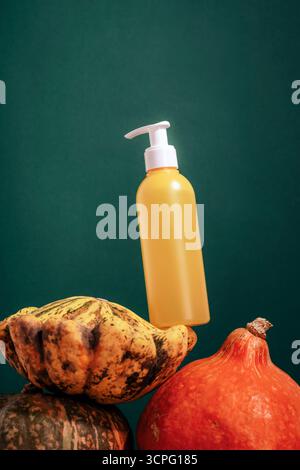 Gelbe Pumpflasche, die zwischen Kürbissen vor dunkelgrünem Hintergrund steht, minimale Zusammensetzung für die Präsentation von Kosmetik- oder Hautpflegeprodukten. Modell. Stockfoto