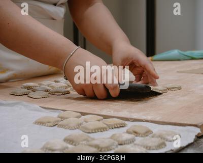 In den Händen junger Frauen wird fachmännisch traditionelle italienische gefüllte Pasta-Tortelli in einer professionellen Küche hergestellt, die kulinarische Fähigkeiten und Hingabe zum Ausdruck bringt Stockfoto