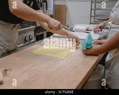 In einer hellen und modernen, professionellen Küchenumgebung bereiten erfahrene Köche sorgfältig traditionelle italienische Tortelli-Pasta aus frischen Zutaten von Hand zu Stockfoto