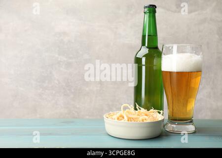 Getrocknete Tintenfischspäne und Bier auf hellblauem Holztisch vor grauem Hintergrund, Nahaufnahme. Leerzeichen für Text Stockfoto