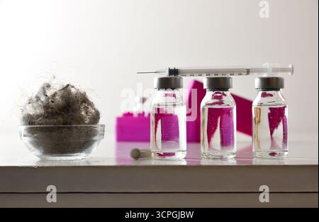 Staubmilbenimpfkonzept mit mehreren Durchstechflaschen mit Impfstoffdosen und einer Spritze oben und einem lila Behälter mit Behandlungsflaschen dahinter auf A Stockfoto