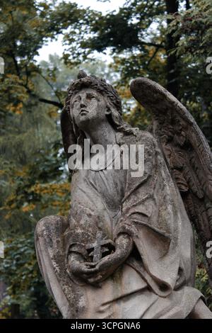 Der antike Steinengel hält eine Schüssel, mit traurigem Ausdruck, der Themen wie Erinnerung, Trauer und spirituelle Hingabe reflektiert. Hochwertige Fotos Stockfoto
