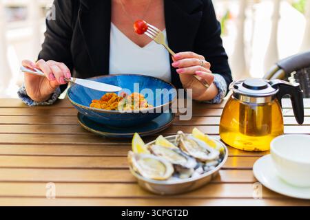 Frau sitzt am Esstisch und hält Besteck, wirbelt frisch servierte Spaghetti-Bolognese und genießt ihre Mahlzeit im Restaurant Stockfoto