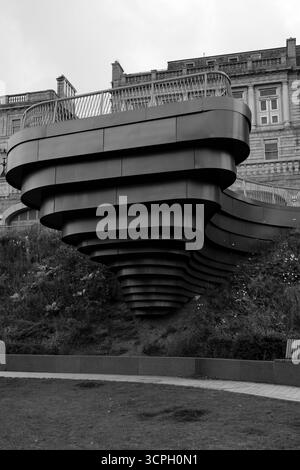 Eine markante moderne, geschichtete Architektur, die einem wirbelnden Wirbel ähnelt, erhebt sich auf einem grasbewachsenen Hügel vor einem klassischen Gebäude in Blac Stockfoto