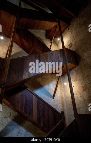Eine spiralförmige Holztreppe in einem Steingebäude, beleuchtet von sanften Lichtern, die architektonische Gestaltung und Textur zeigen Stockfoto
