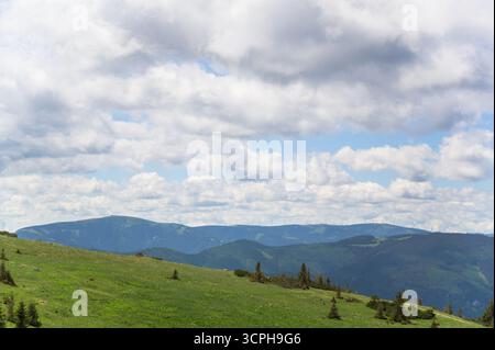 Der atemberaubende Blick auf die Rax Mountains bietet weitläufige grüne Hügel unter einem hellblauen Himmel voller flauschiger weißer Wolken und Sonnenlicht casti Stockfoto